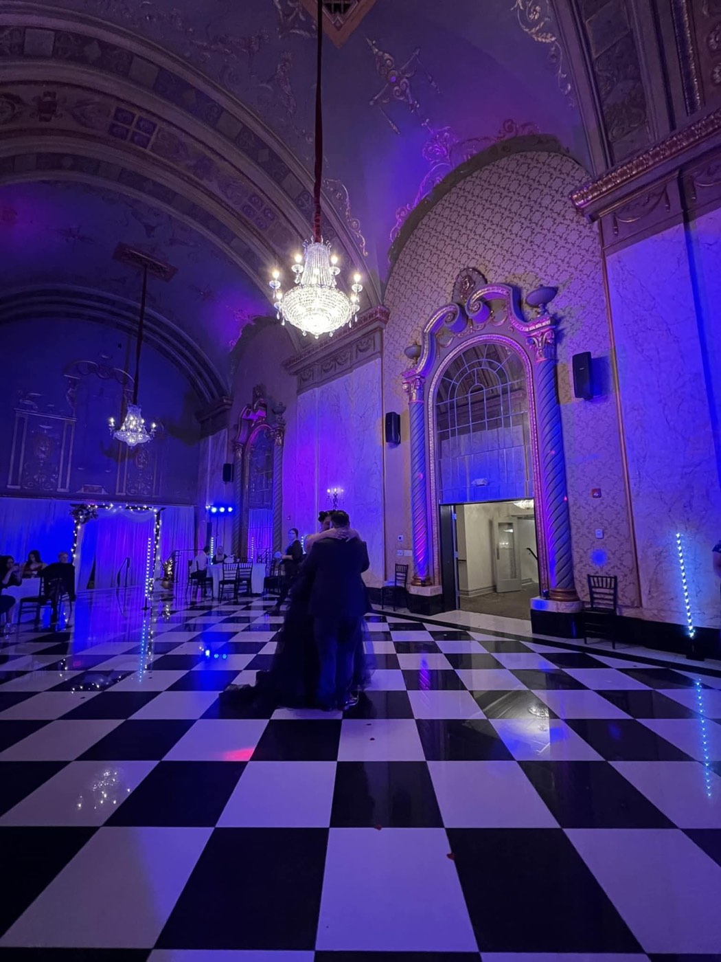 A grand hall with a checkered dance floor washed in purple